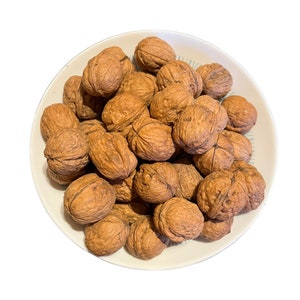 Pode incluir: Uma tigela cheia de uma grande pilha de nozes marrons. As nozes estão em uma tigela branca com um padrão azul e branco.