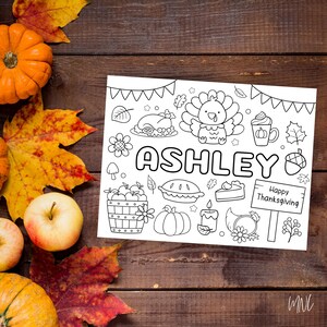 May include: A black and white Thanksgiving-themed coloring page with the name "Ashley" in large letters. The page features illustrations of a turkey, pie, pumpkins, and the text "Happy Thanksgiving". The page is surrounded by fall leaves, apples, and pumpkins.