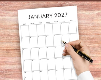 May include: A white paper calendar for January 2027 with black text and grid lines. The calendar features the month and year at the top, followed by days of the week and numbered dates from 1 to 31. A black pen is positioned over the paper.