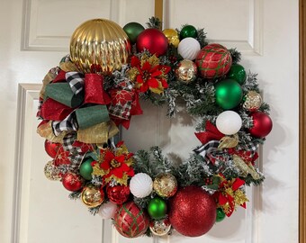 May include: A festive Christmas wreath with a variety of ornaments. The wreath features a large gold ball, red and green ornaments, white and gold accents, and red poinsettias. Green and red ribbons add to the holiday theme.