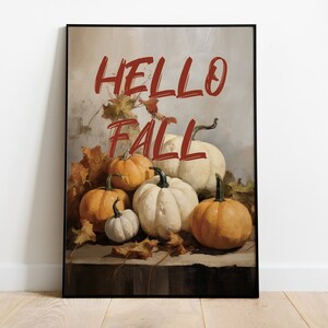 Könnte beinhalten: Ein gerahmter Druck mit einem Gemälde eines Stilllebens mit Kürbissen und Herbstblättern. Der Text "HELLO FALL" ist in Rot auf dem Druck geschrieben.