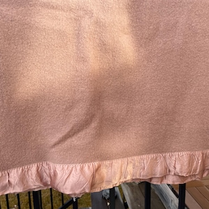 Peut inclure: Une couverture rose poudré avec une surface texturée. Le bord inférieur présente une garniture froissée en satin de couleur rose clair. La couverture est drapée sur une balustrade.