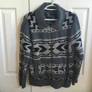 May include: A grey and black patterned sweater with a zip closure. The sweater has a geometric design with black and white accents.
