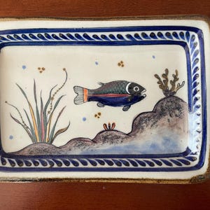 May include: Rectangular ceramic dish with a hand-painted underwater scene. The design features a fish, seaweed, and coral against a cream background. The border is a blue and white pattern. The dish is approximately 20 cm long and 15 cm wide.