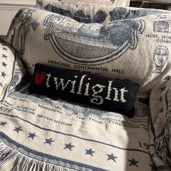 Peut inclure: Un coussin rectangulaire en crochet noir orné d'un petit cœur rouge et du mot "twilight" brodé en lettres blanches au centre. Le coussin présente une texture en fil et est disposé horizontalement.