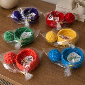 May include: Six sets of crocheted bowls and matching spheres, each individually wrapped in clear plastic with a gold twist tie. The sets come in purple, red, green, yellow, orange, and blue, with a small decorative card inside each bowl.