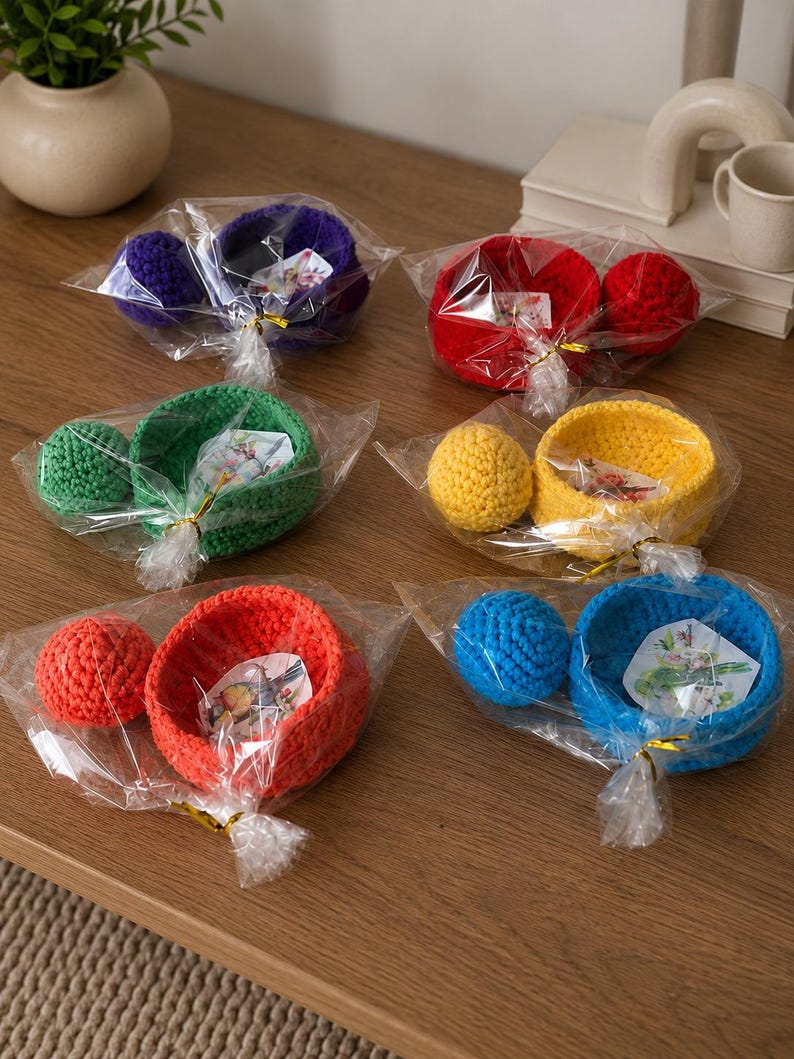 May include: Six sets of crocheted bowls and matching spheres, each individually wrapped in clear plastic with a gold twist tie. The sets come in purple, red, green, yellow, orange, and blue, with a small decorative card inside each bowl.