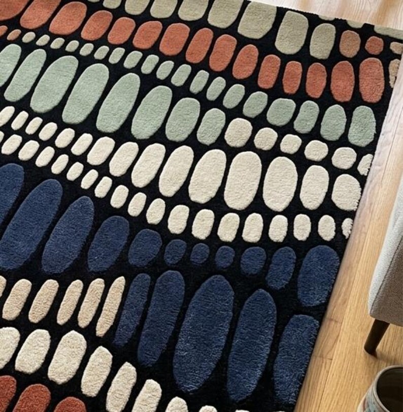 K&ouml;nnte beinhalten: Ein gemusterter Teppich mit schwarzem Hintergrund und Reihen ovaler Formen in verschiedenen Farben. Die Farben umfassen Wei&szlig;, Blau, Orange und Gr&uuml;n. Der Teppich besteht aus einem weichen, strukturierten Material.