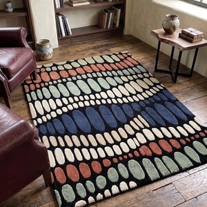 K&ouml;nnte beinhalten: Ein rechteckiger Teppich mit schwarzem Hintergrund und einem Muster aus farbigen, ovalen Formen in Orange, Gr&uuml;n, Blau und Creme. Der Teppich liegt auf einem Holzboden und verleiht dem Raum W&auml;rme. Ma&szlig;e in Zentimetern.