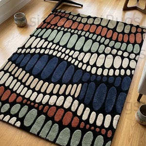 K&ouml;nnte beinhalten: Rechteckiger Teppich mit einem Muster aus l&auml;nglichen Ovalen in verschiedenen Farben, darunter Orange, Gr&uuml;n, Wei&szlig;, Beige und Marineblau, auf schwarzem Hintergrund. Der Teppich liegt auf einem Holzboden.