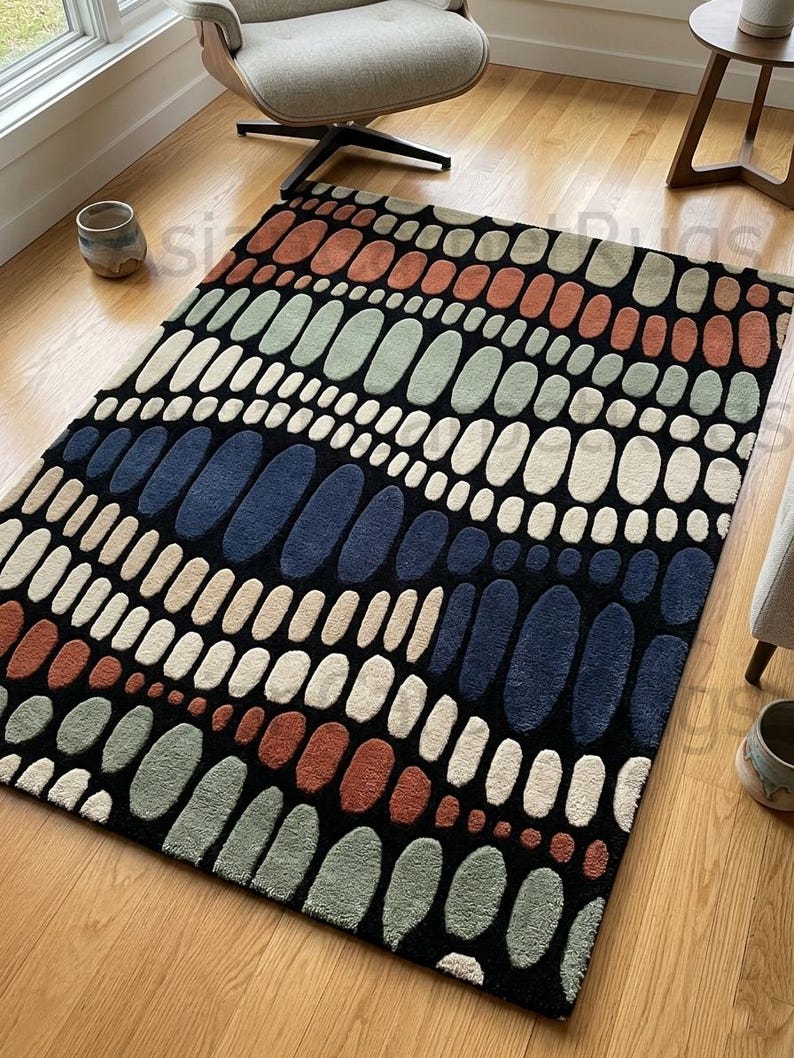 K&ouml;nnte beinhalten: Rechteckiger Teppich mit einem Muster aus l&auml;nglichen Ovalen in verschiedenen Farben, darunter Orange, Gr&uuml;n, Wei&szlig;, Beige und Marineblau, auf schwarzem Hintergrund. Der Teppich liegt auf einem Holzboden.