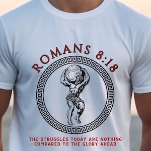 May include: White t-shirt with a black and white graphic of a man holding a globe. The graphic is surrounded by a red circle with the text "ROMANS 8:18" in black. Below the graphic is the text "THE STRUGGLES TODAY ARE NOTHING COMPARED TO THE GLORY AHEAD" in black.