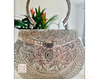 May include: A silver metal clutch purse with an ornate floral design and a top handle. The purse has a hinged clasp and a decorative floral pattern.