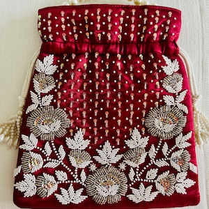 May include: A burgundy velvet drawstring bag with a floral design embroidered with white and silver beads and sequins.