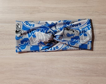 May include: A gray and blue headband with a checkered pattern and the words "Detroit Lions" repeated throughout.