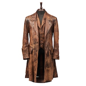 K&ouml;nnte beinhalten: Ein brauner Ledercoat und Weste-Set, pr&auml;sentiert auf einer Holzpuppe. Der lange Coat hat eine Used-Optik, einen Reverskragen und Vordertaschen. Die gekn&ouml;pfte Weste ist darunter sichtbar. Das Set ist im Vintage-Stil gehalten.