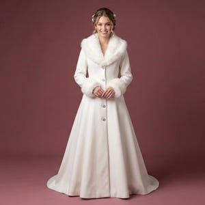 Puede incluir: Un abrigo de novia largo y blanco con cuello y pu&ntilde;os de piel sint&eacute;tica. El abrigo tiene una botonadura frontal y una falda fluida. La novia sonr&iacute;e. El fondo es rojo liso y apagado. Adecuado para una boda.