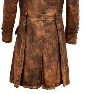 May include: A brown leather coat with a distressed finish. The coat features long sleeves, button details, and a split back design. The leather has a worn, textured appearance, suggesting a vintage or rugged style. The coat is a medium length.