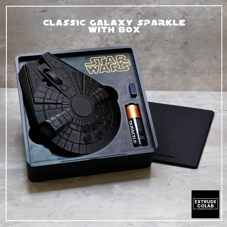 May include: A black 3D-printed Millennium Falcon model inside a square display box with the Star Wars logo in gold. The set includes a Duracell battery and a separate black lid. The text CLASSIC GALAXY SPARKLE WITH BOX is printed above the box.