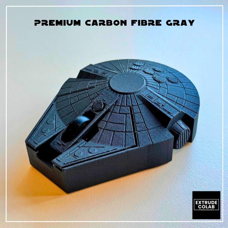May include: A dark gray, textured, 3D-printed model of a spaceship with a circular main body and a forward-projecting cockpit. The text "PREMIUM CARBON FIBRE GRAY" is printed above the object, and a logo for "EXTRUDE COLAB" is in the corner.