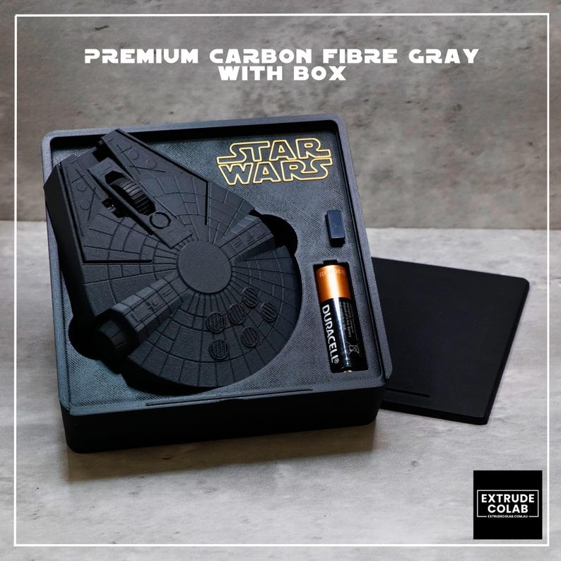 May include: A matte gray computer mouse shaped like the Millennium Falcon from Star Wars, housed in a custom black tray with a Duracell battery. The text PREMIUM CARBON FIBRE GRAY WITH BOX is visible at the top, and the Star Wars logo is printed in gold.