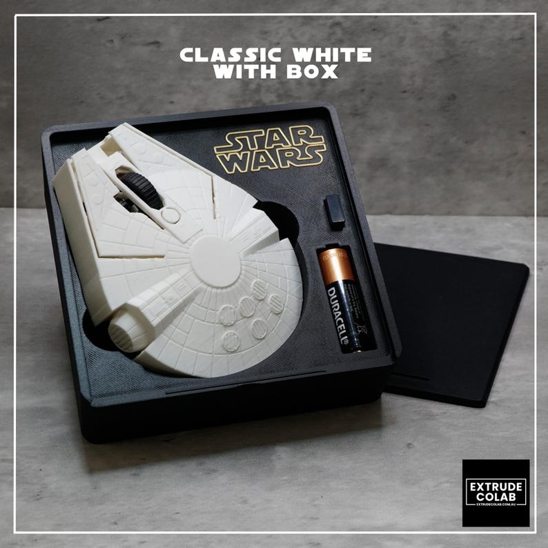 May include: A white computer mouse shaped like the Millennium Falcon from Star Wars, housed in a black rectangular box with a gold Star Wars logo. The set includes a black Duracell battery and a small black component, all arranged in a custom tray.