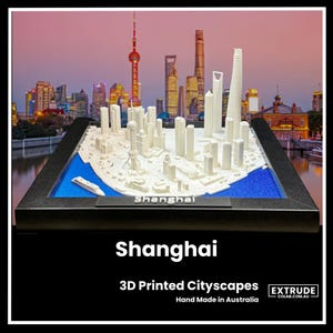 Pode incluir: Um modelo de cidade de Xangai, China, impresso em 3D. O modelo é branco e está colocado em uma moldura preta com uma base azul. O modelo é feito à mão na Austrália. O texto "Shanghai" está impresso na base do modelo.
