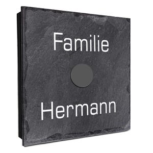Peut inclure: Une plaque carrée en ardoise gris foncé avec le mot "Familie" au-dessus de "Hermann" en lettres blanches. Un bouton circulaire gris foncé est centré sur la plaque. Il s'agit probablement d'un numéro de maison ou d'une plaque nominative.