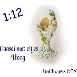 May include: A white ceramic egg with a nest of colourful Easter eggs inside, decorated with pastel flowers and green leaves. The egg is on a white pedestal with a delicate lace design. The text "1:12" is in the top left corner of the image. The text "Paasei met eitjes Hoog" is in the bottom left corner of the image. The text "Dollhouse DIY" is in the bottom right corner of the image.