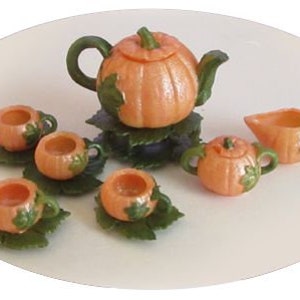 Op de afbeelding: Een miniatuur theeservies met een pompoen-thema, met een theepot, roomkan, suikerpot en vier kopjes en schoteltjes. De set is gemaakt van oranje en groen plastic en heeft een pompoenontwerp met bladeren.