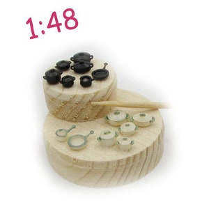 Op de afbeelding: Een miniatuurset van zwarte en witte potten en pannen op een houten platform. De set bevat een verscheidenheid aan maten en stijlen van potten en pannen, en een houten lepel. De tekst "1:48" is op de afbeelding gedrukt.