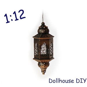 May include: A bronze-colored, ornate lantern with intricate cut-out patterns. The lantern is suspended by a thin wire and features a decorative top and bottom. The text "1:12" and "Dollhouse DIY" are visible.