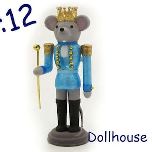 Pode incluir: Uma figura de quebra-nozes de bricolage para casa de bonecas na escala 1:12. O quebra-nozes é um rato que usa um uniforme azul com guarnições douradas e uma coroa dourada. O rato segura um pau com ponta dourada.