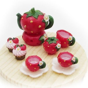 Può includere: Un set da tè in miniatura a tema fragola su una base in legno. Il set comprende una teiera, una zuccheriera, due tazze e piattini da tè e due cupcake a forma di fragola.