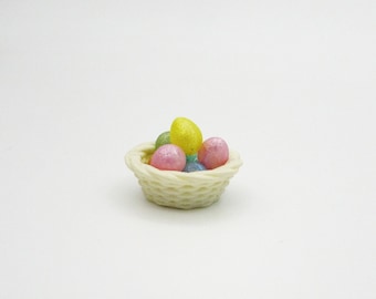 May include: A small white wicker basket filled with colorful Easter eggs. The eggs are pink, blue, green, and yellow.