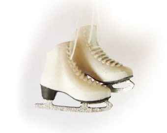 May include: A pair of white ice skates with black accents and silver blades. The skates are tied together with a white string.