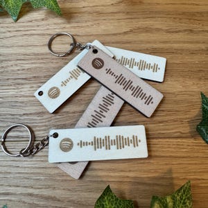 Op de afbeelding: Vier houten sleutelhangers met een Spotify-logo en een uniek barcode-ontwerp. De sleutelhangers zijn lichtbruin en wit.