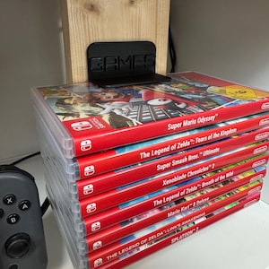 Könnte beinhalten: Ein Stapel Nintendo Switch-Videospielkassetten, darunter Super Mario Odyssey, The Legend of Zelda: Tears of the Kingdom, Super Smash Bros. Ultimate, Xenoblade Chronicles 2, The Legend of Zelda: Breath of the Wild, Mario Kart 8 Deluxe, The Legend of Zelda: Link's Awakening und Splatoon 2.