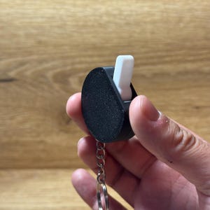 Può includere: Un portachiavi nero con uno slider bianco. Il portachiavi ha la forma di una lacrima e ha una catena argentata.
