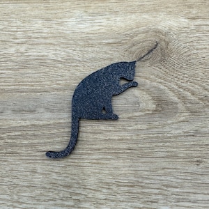 May include: Black silhouette of a cat sitting on a wood background.