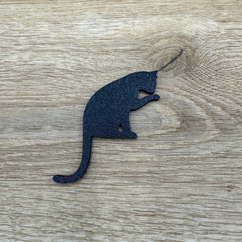 May include: Black silhouette of a cat sitting on a wood background.