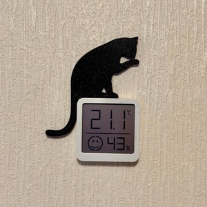 May include: A black cat silhouette with a white digital thermometer displaying 21.1 degrees Celsius and 43% humidity.
