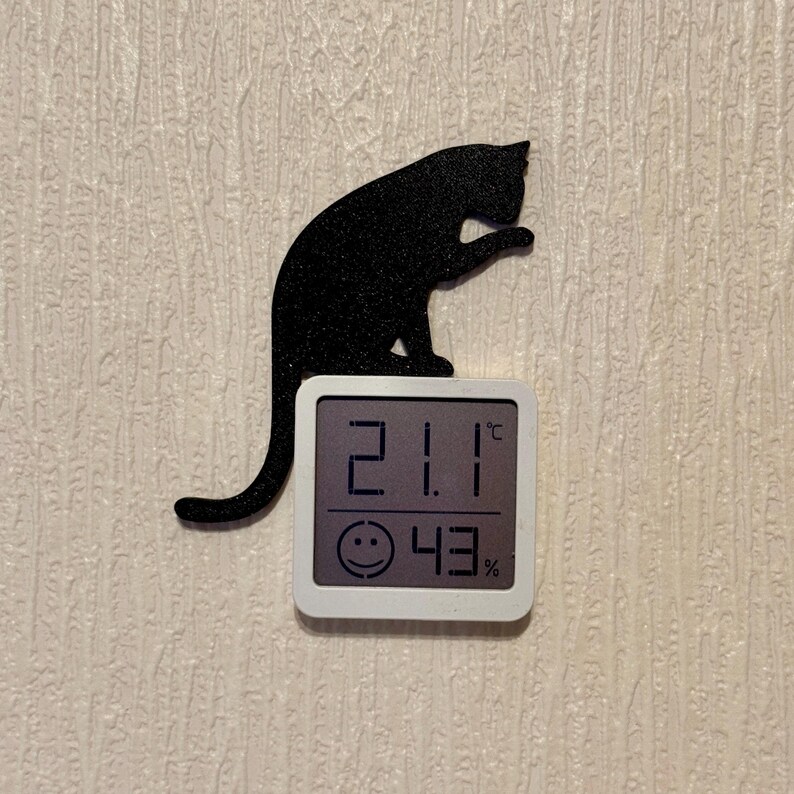 May include: A black cat silhouette with a white digital thermometer displaying 21.1 degrees Celsius and 43% humidity.