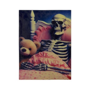 May include: A decorative chopping board showing a skeleton in a bed with a teddy bear. The skeleton wears a headband and is covered by a pink blanket. The bed has a pink pillow and a white headboard.