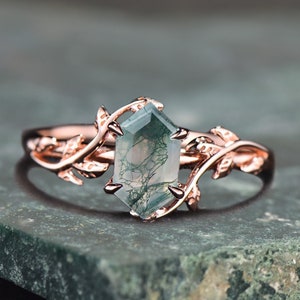 Peut inclure: Bague en or rose ornée d'une pierre de moss agate hexagonale. La monture de la bague est ornée d'un motif de vigne et de feuilles. La pierre précieuse présente un motif vert et blanc.