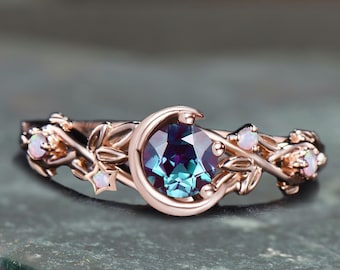 May include: A rose gold ring with a crescent moon design and a blue-green gemstone. The ring is adorned with delicate leaves and small white gemstones.