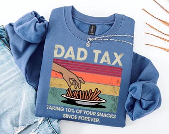 May include: A blue sweatshirt with a vintage-style graphic that says "Dad Tax" and features a hand reaching for a plate of french fries. The text below the graphic says "Taking 10% of your snacks since forever."
