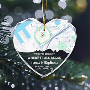 May include: Heart-shaped clear glass ornament with a map design and gold string. The ornament features the text "SEPTEMBER 22ND 2022 WHERE IT ALL BEGAN Tomas & Stephanie 100 ALFRED LERNER WAY CLEVELAND, OHIO 44114".