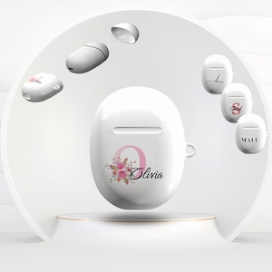 Könnte beinhalten: Weißes Airpod-Case mit einem Blumenmuster und dem Namen Olivia darauf gedruckt. Das Case steht auf einem weißen Sockel. Im Hintergrund sind weitere Airpod-Cases mit verschiedenen Designs zu sehen.