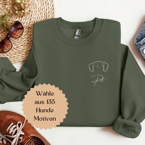 Könnte beinhalten: Ein olivgrünes Sweatshirt mit einer weißen Umrisszeichnung von Hundeohren und dem Wort "Pet" in Schreibschrift. Das Sweatshirt hat einen Rundhalsausschnitt und lange Ärmel. Ein beigefarbenes Schild mit gezacktem Rand und deutschem Text befindet sich in der unteren linken Ecke.